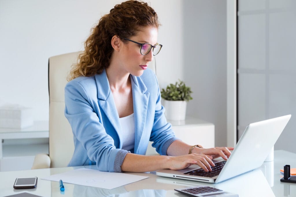 A imagem mostra uma mulher, responsável pelas finanças da ONG, sentada em seu escritório. Ela está em frente ao computador, pesquisando a melhor conta digital para ONGs.