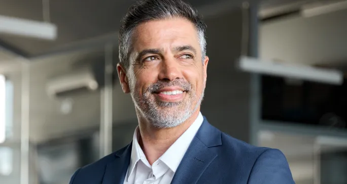 Homem grisalho de terno sorri por fazer bom trabalho de gestão de negócios.