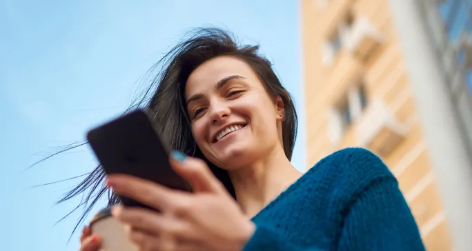 Mulher com cabelos ao vento, segura o celular e sorri após fazer Pix.